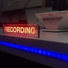 photo of a recording studio desk with an illuminated light showing someone is recording inside