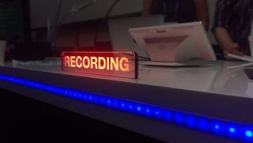 photo of a recording studio desk with an illuminated light showing someone is recording inside