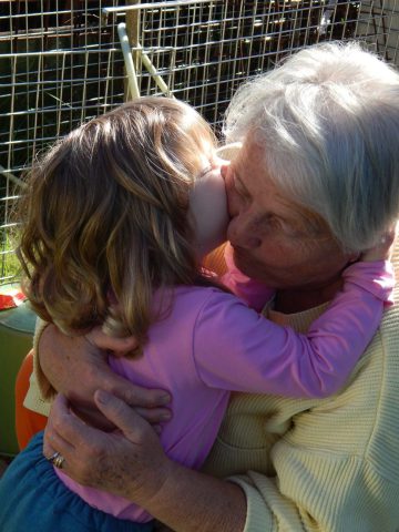 white grandma holding her five year old grand-daughter in her arms while she kisses her and hugs her neck back