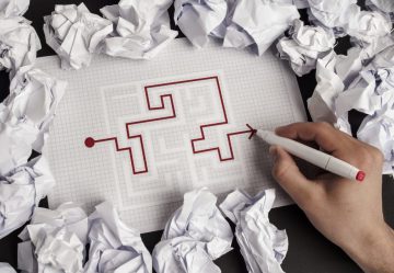 puzzle maze on paper with a red line showing the completion from one end to the other crumpled papers scattered all around the table