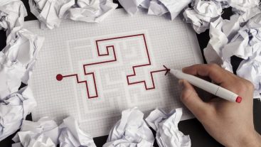 puzzle maze on paper with a red line showing the completion from one end to the other crumpled papers scattered all around the table
