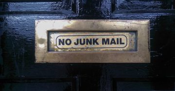 black door with a metal mail slot reading the words "no junk mail" to represent spam