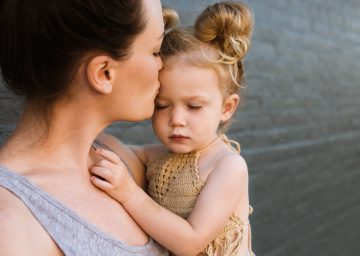 young twenty something Mom kissing her two year old daughter on the forhead while holding her in her arms