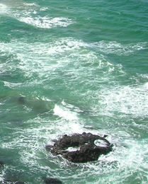 a black rock sits among the blue rocky waves of the Pacific Ocean