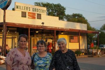 grandma dressed in a black print shirt in her eighties with daughter wearing a blue shirt in her sixties and grad-daughter dressed in a pink blouse in her forties