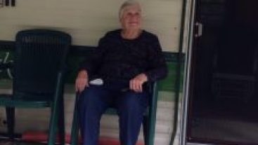 elderly grandmother wearing a black shirt sitting on a trailer porch in a green chair