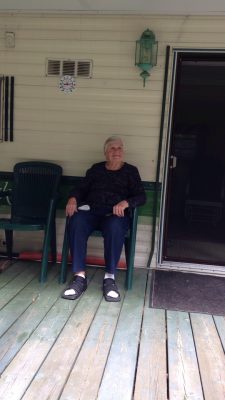 elderly grandmother wearing a black shirt sitting on a trailer porch in a green chair