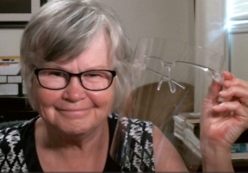 elderly woman wearing black glasses showing a pair of safety glasses to others