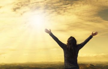 brown haired woman with arms stretched out to heaven and sunshining through clouds