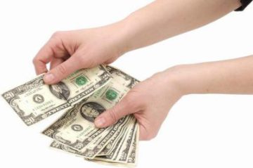 young lady hands holding American twenty dollar bills and giving them out to someone