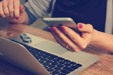 young woman hands with painted nails holding an iphone with her laptop in front of her