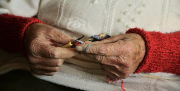 elderly grandma hands crocheting with small yellow hook and blue yarn