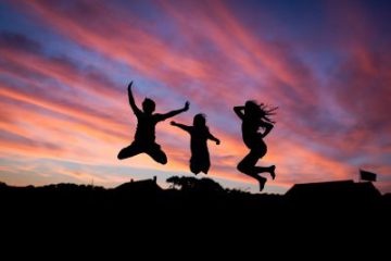 black silhouttes of two girls and a boy jumping up with pretty pink sunset in the background