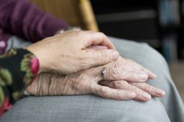 elderly mother's hands folded on leg with daughter's hand over top