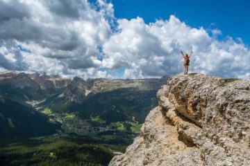 woman with arms raised standing on top of a mountain peak she just successfully climbed