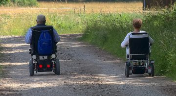 elderly man and woman driving powered scooter wheelchairs