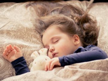 cute two year old girl with long brown hair sleeping in bed with her pink stuffed rabbit