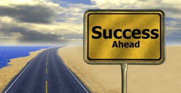 picture of a grey highway surrounded by sand and a sky with clouds highway sign says success ahead