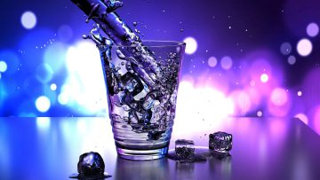 spout pouring out water into a glass with ice cubes on the table beside it